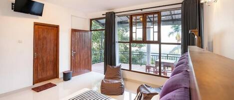 Ein modernes Hotelzimmer mit großem Fenster, einem an der Wand befestigten Flachbildfernseher, einer Holztür und einem Balkon mit Gartenmöbeln.