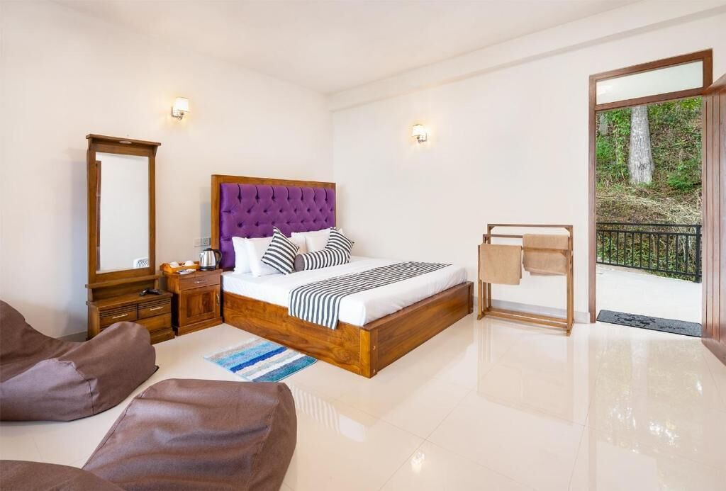 Une chambre avec un grand lit, une table de chevet en bois, une commode, un miroir, un banc et une vue sur l’extérieur.