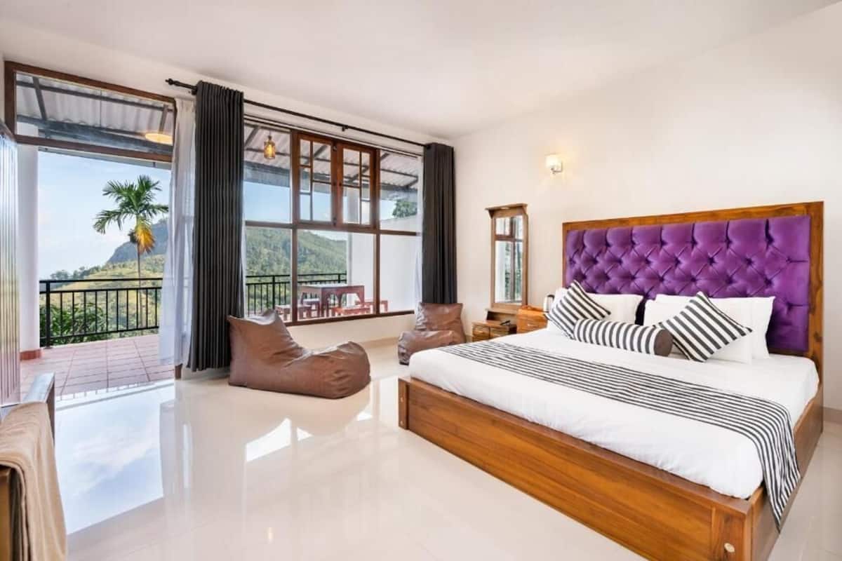 A spacious bedroom with a large bed, a view of the outdoors, and a balcony with seating.