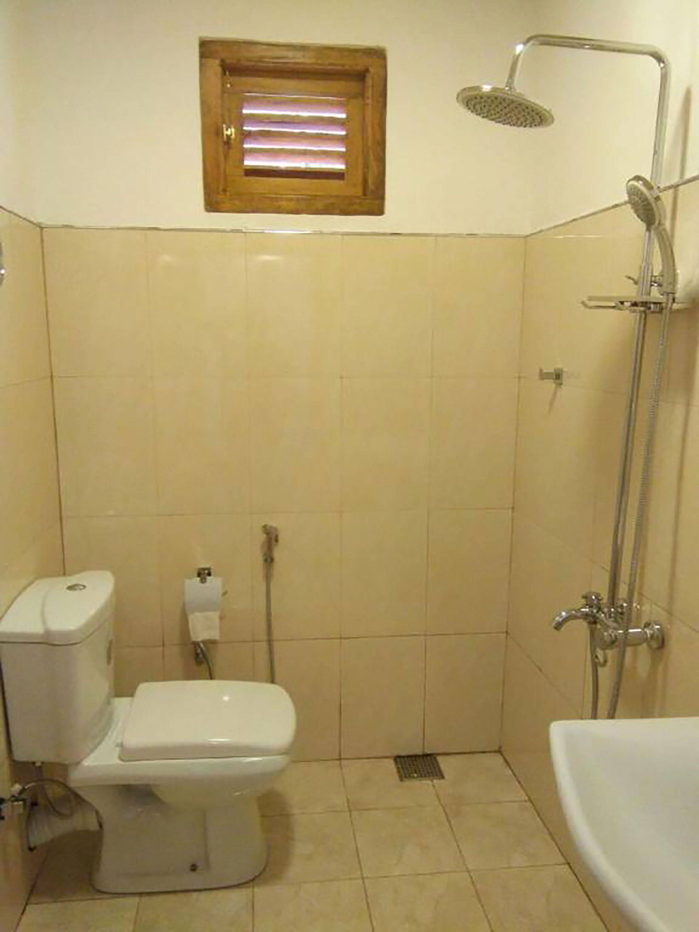 A small bathroom with a toilet, a shower, and a window.