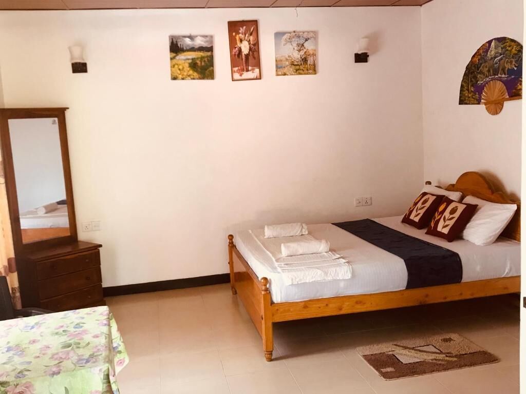 Une chambre à coucher avec un lit en bois, une commode et un miroir. Quatre tableaux encadrés sont accrochés au mur.
