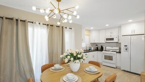 Une cuisine moderne avec des meubles blancs, un îlot central agrémenté d’un vase de fleurs et un coin repas avec une table ronde et des chaises.