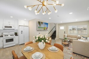 A modern kitchen with white cabinets, a built-in microwave, and a gas stove. There is a dining area with a wooden table set for four, surrounded by orange chairs. A large vase with white flowers is placed on the table. - Outstanding 2beds/2baths Home Close to Pier/Beach (Huntington beach)