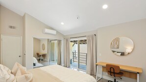 Une chambre à coucher avec un lit, un bureau et une chaise. Il y a une fenêtre avec des rideaux et un balcon.