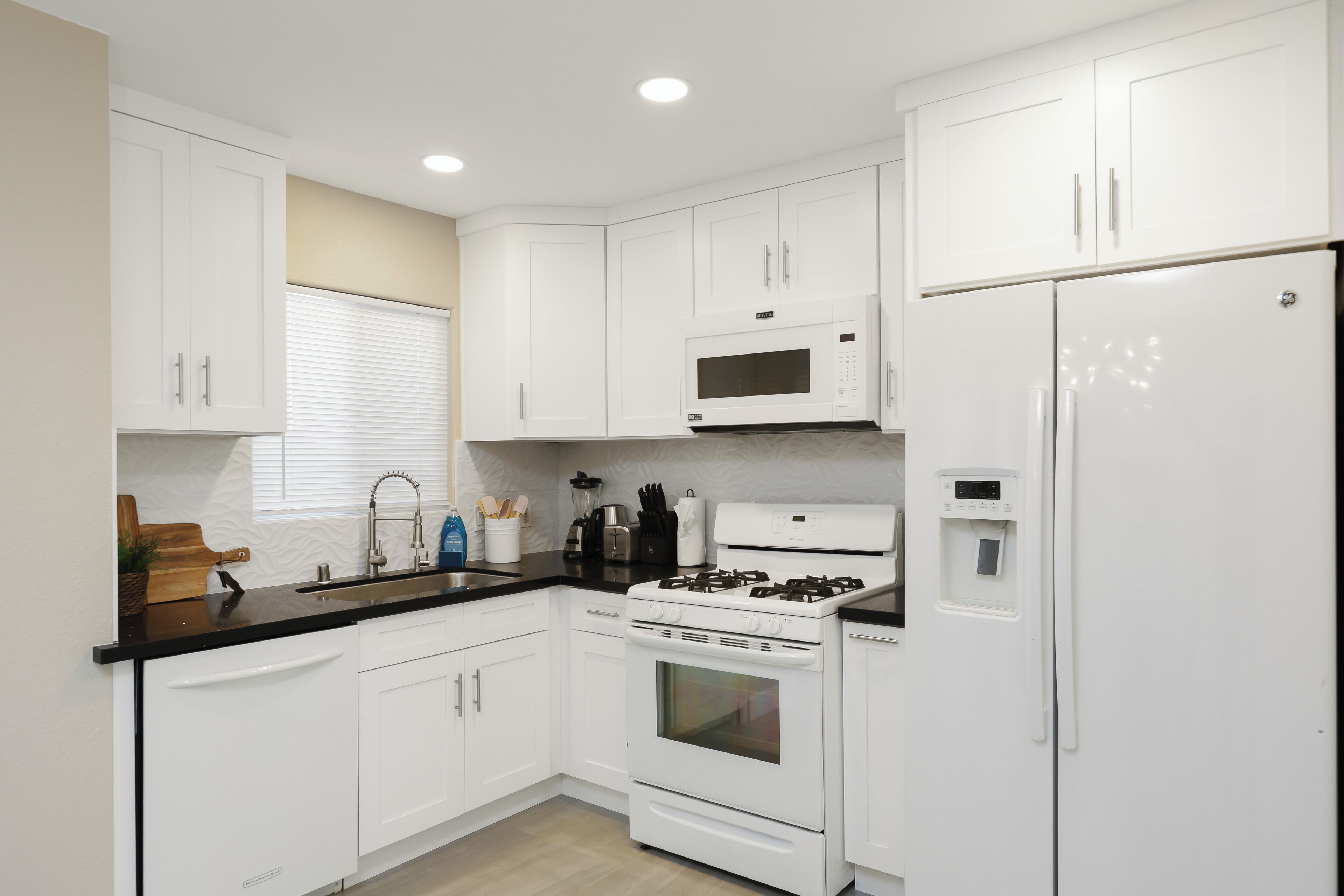 Una cocina moderna con armarios blancos, encimera negra, microondas, estufa y refrigerador.