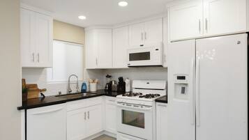Una cocina moderna con armarios blancos, encimera negra, microondas, estufa y refrigerador.