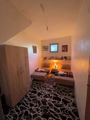 Een kleine kamer met een bed, nachtkastje, lamp, kast en raam.