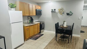A compact kitchen with wooden cabinets, a refrigerator, microwave, and a dining area with a table and chairs. - Exquisite private 1-bedroom apartment in delightful Newark with modern amenities (Newark)