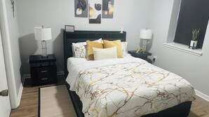 A bedroom with a bed, bedside tables, a nightstand, a window with a plant, and artwork on the wall. - Exquisite private 1-bedroom apartment in delightful Newark with modern amenities (Newark)