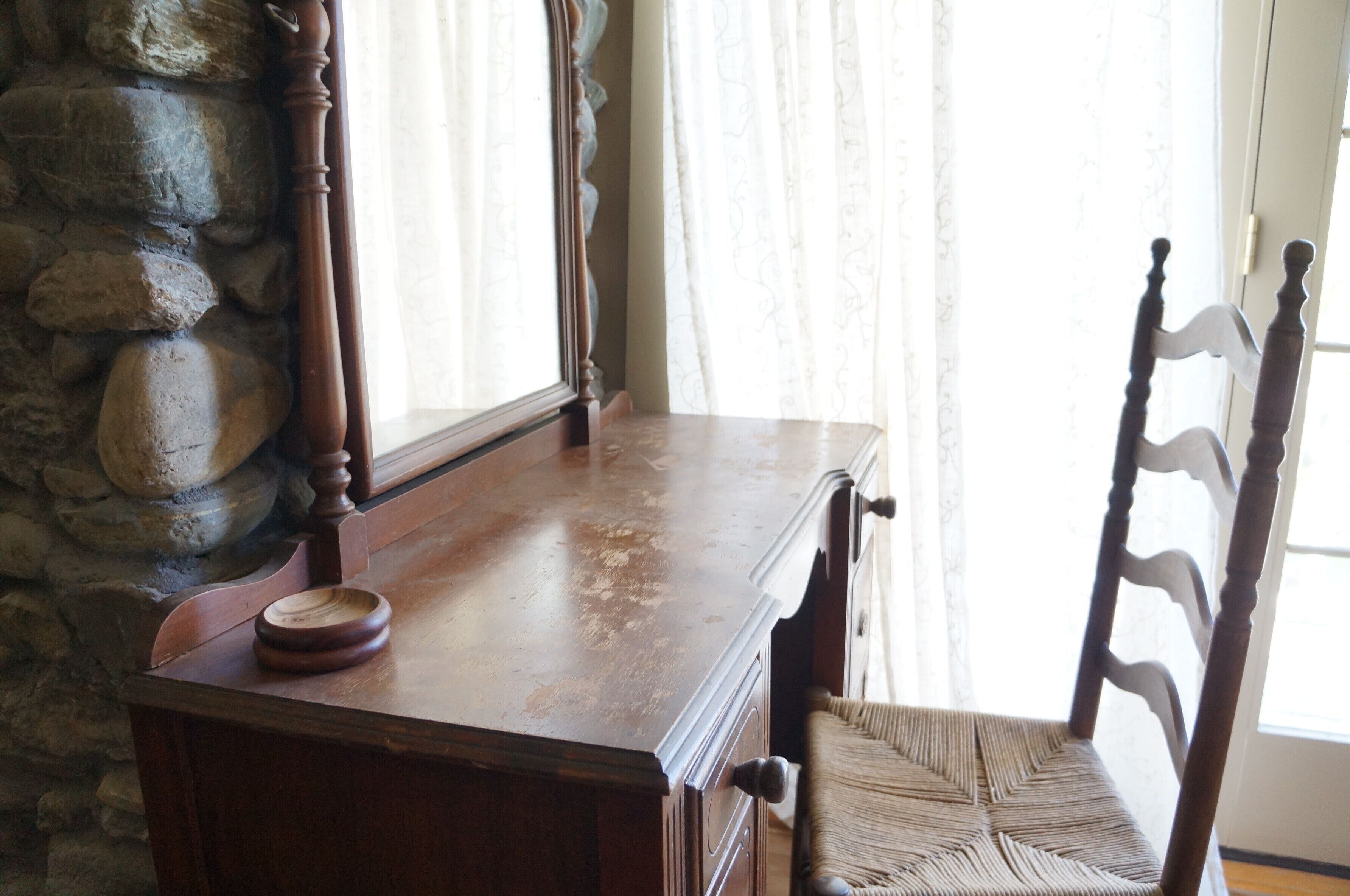 A wooden desk with drawers, a woven chair, and a stone wall.