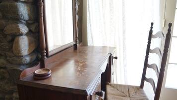 A wooden desk with drawers, a woven chair, and a stone wall.