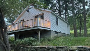 A two-story house with a balcony, stone wall, and surrounding trees. - Countryside Cottage with Sauna and Fireplace (Berlin)