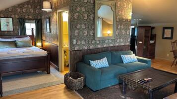 Ein Zimmer mit einem Bett, einem Schlafsofa, einem Couchtisch und einem Spiegel. Eine Tür führt zu einem Badezimmer.