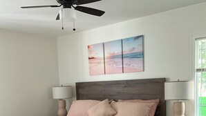 A bedroom with a bed, nightstands, a ceiling fan, a wall-mounted artwork, and a window.