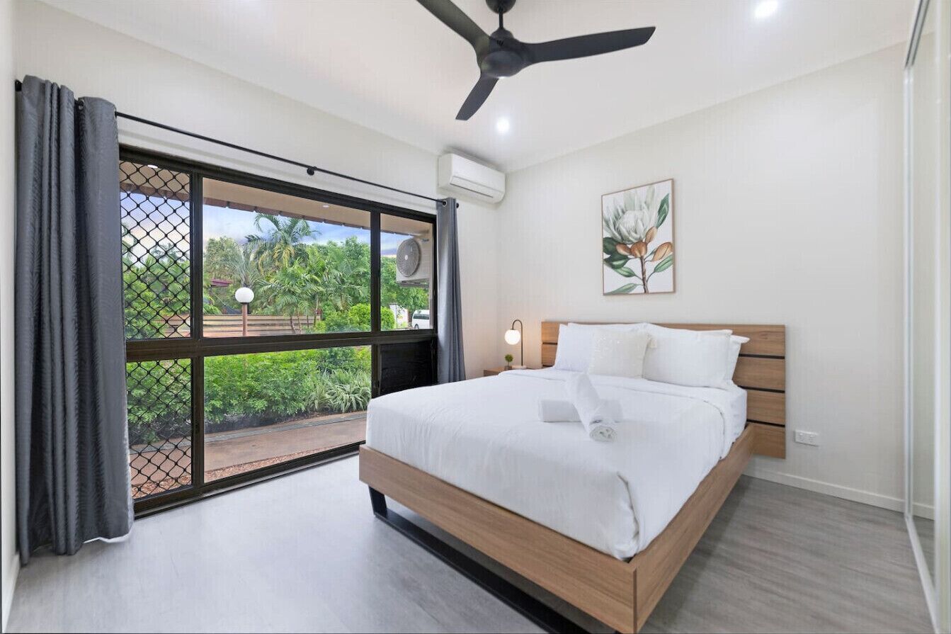 A bedroom with a bed, a ceiling fan, a window with curtains, and a wall-mounted air conditioner.