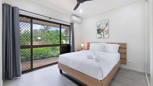 Ein Schlafzimmer mit Bett, Deckenventilator, einem fenster mit Vorhängen und einer Wand-Klimaanlage.