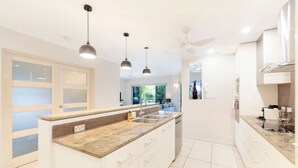 A modern kitchen with white cabinetry, a granite countertop, a built-in oven, and a ceiling fan.