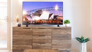 A flat-screen TV on a wooden cabinet with a Sydney Opera House image displayed.