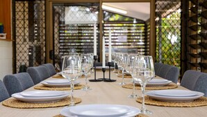 Une table à manger dressée avec des assiettes et des verres à vin, entourée de chaises, dans une pièce offrant une vue à travers une fenêtre à motifs.