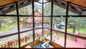 Une cabane dotée d’une grande fenêtre en verre, d’une terrasse en bois et offrant une vue sur une autre cabane située en montagne.
