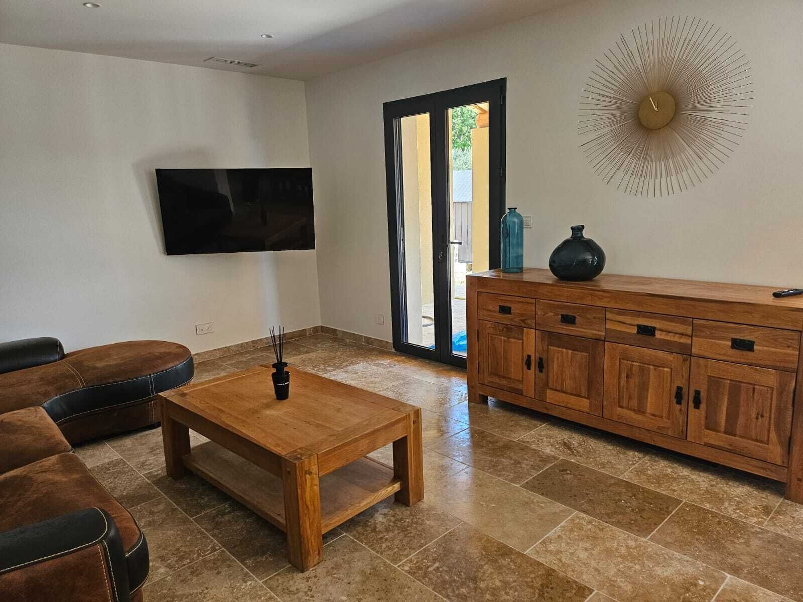 Een woonkamer met een houten salontafel, een leren bank en een aan de muur bevestigde televisie.