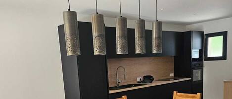 Une cuisine moderne avec un plan de travail noir, des appareils en acier inoxydable et des luminaires suspendus.