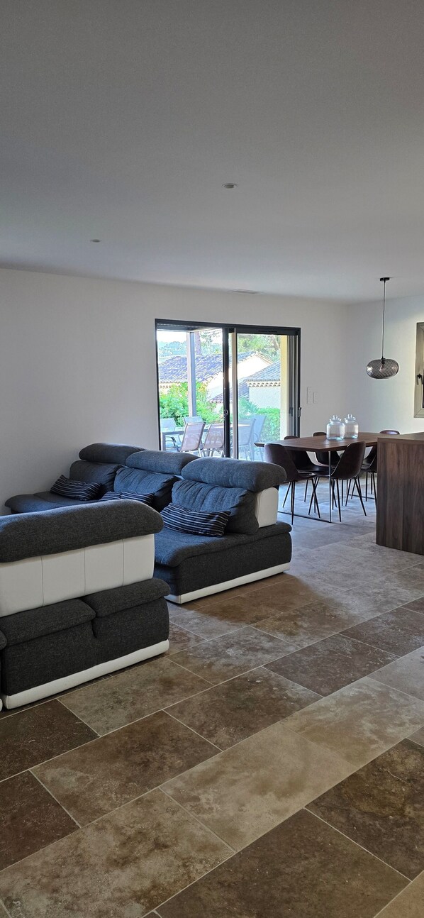 A modern living room with a sectional sofa, a dining area with chairs, and a kitchen area with a counter.