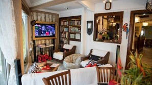 Een gezellige woonkamer met een televisie, boekenplanken, een eethoek met stoelen en een grote spiegel.