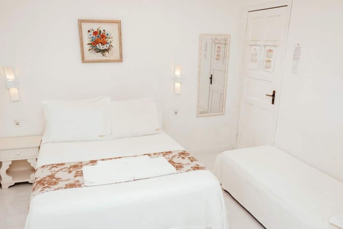 A hotel room with a bed, bedside tables, a nightstand, a door, and a wall-mounted light fixture.