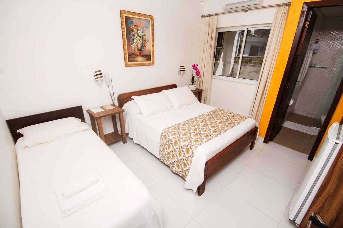 A hotel room with two beds, a painting, a window with curtains, and a door leading to a bathroom.
