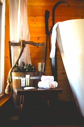 A wooden cabin interior with a rustic chair, a wooden bench, a bathtub, and toiletries on the bench.