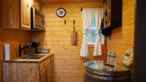 Cozinha compacta com armários de madeira, micro-ondas, pia e janela com cortinas.