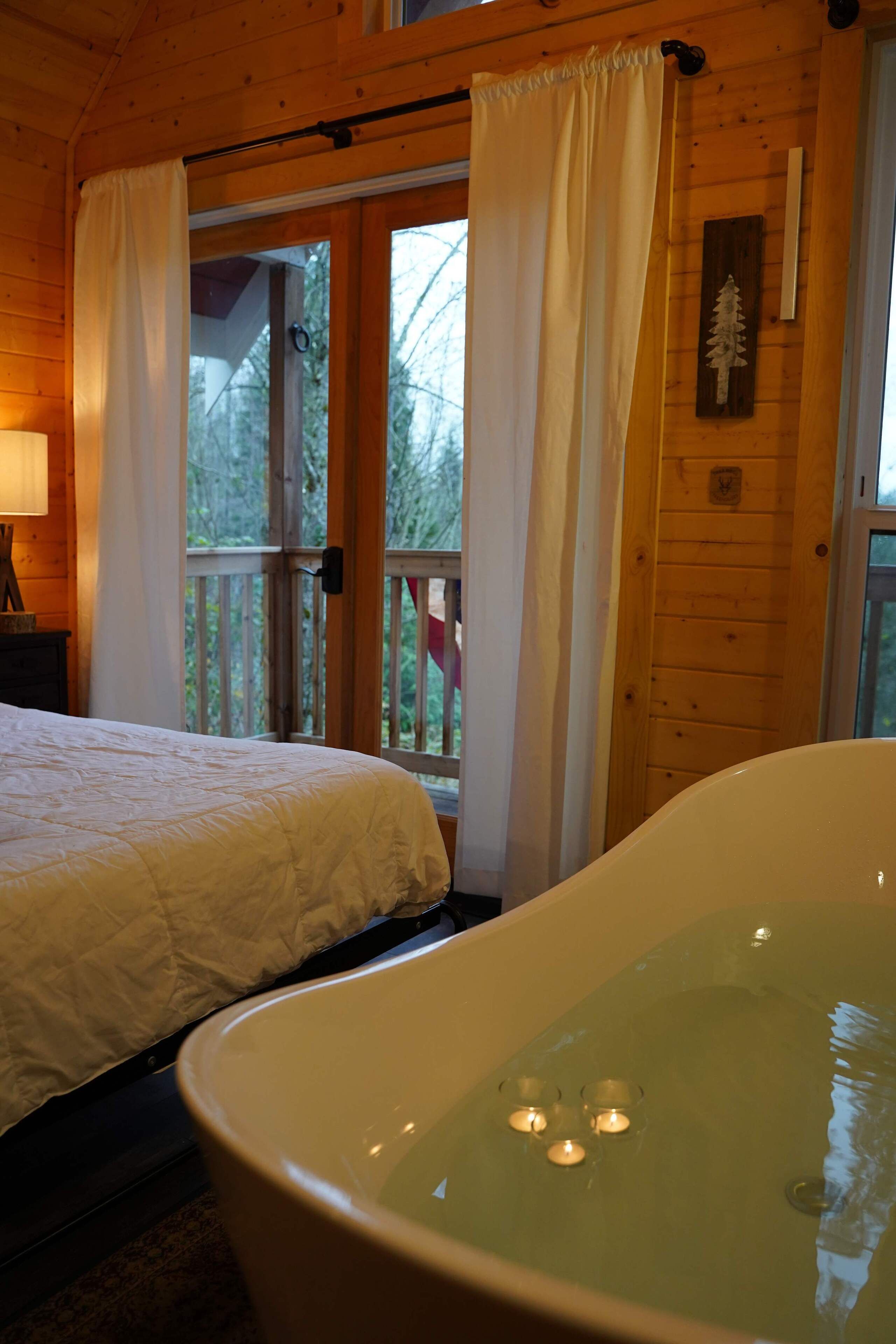 A bedroom with a large bathtub, a bed, and a window with curtains.