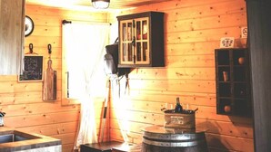 Interior rústico de uma cabana com escada de madeira, fogão central e luminária pendente.