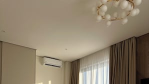 A modern hotel room with a large bed, a sofa, a TV, and an air conditioning unit.