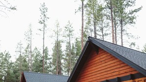 Eine Holzhütte mit großen Fenstern und einer Veranda, auf der ein Stuhl steht.