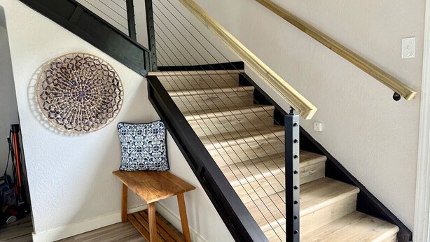 A staircase with black railings and wooden steps, a round wall decoration, and a small wooden bench with a patterned cushion. - DFW Hideaway located right off I-35W and near so many area attractions! (Argyle)