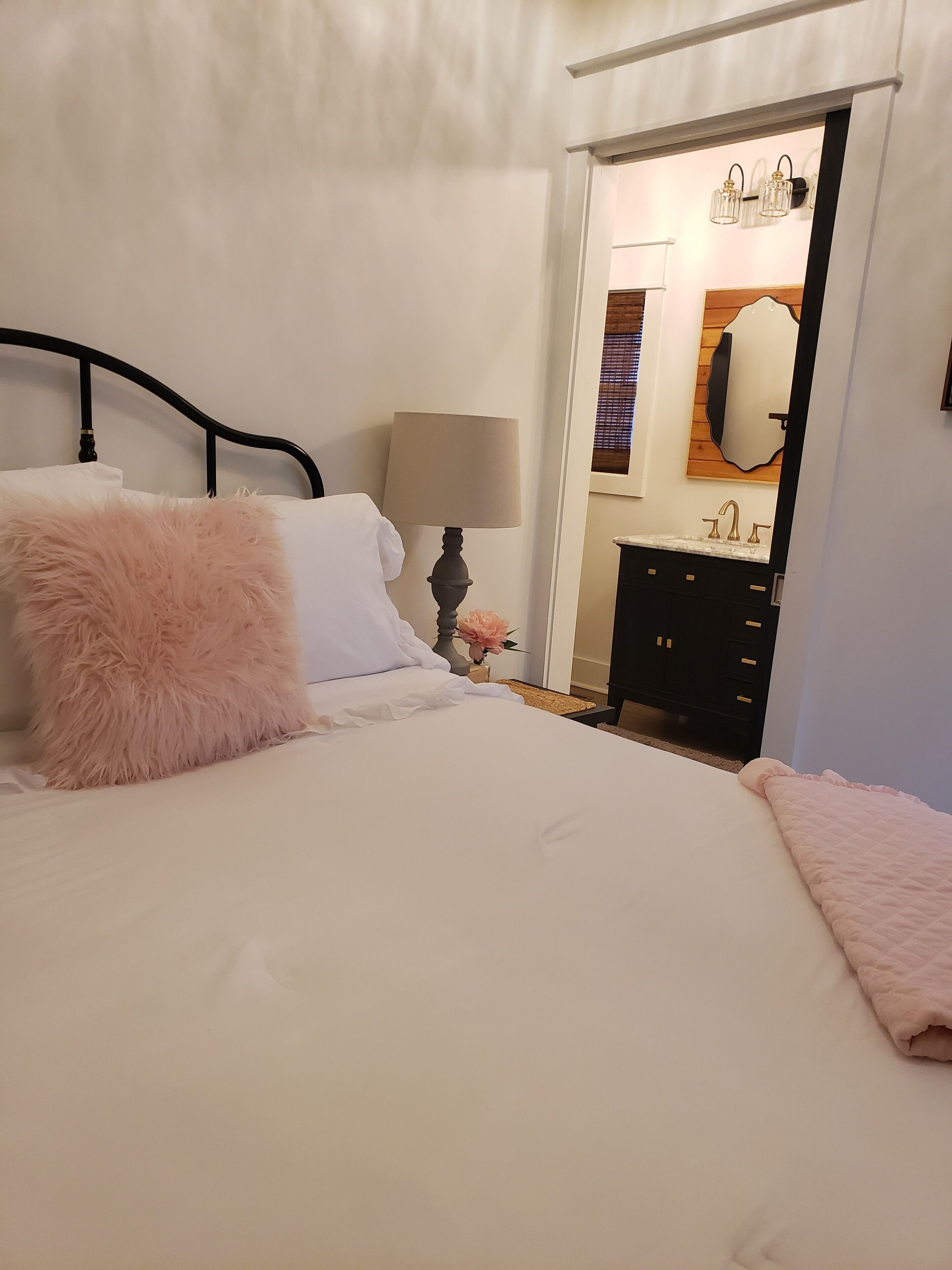 Een slaapkamer met een bed, nachtkastje, lamp, dressoir en spiegel.