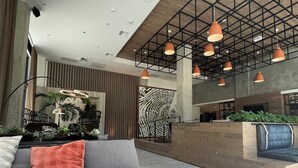 A modern lobby with a sofa, a coffee table, pendant lighting, a reception desk, and a patterned wall.