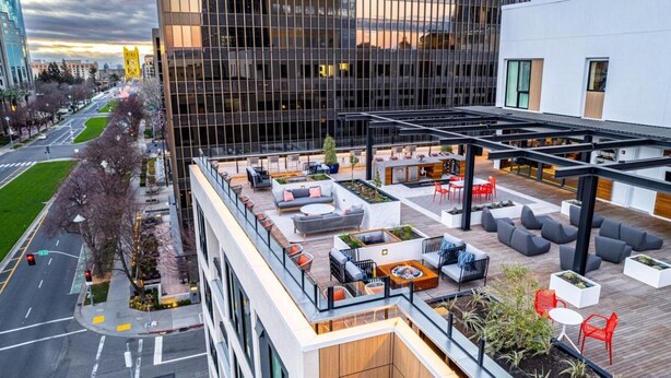 A rooftop patio with outdoor seating, a view of the city, and a modern building in the background.