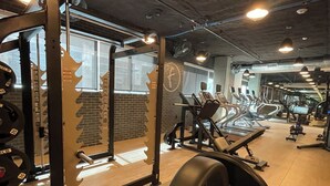 A gym with weightlifting equipment, treadmills, and a brick wall.