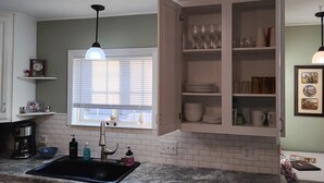 A kitchen with a sink, a window with blinds, a cabinet with dishes, and a coffee maker. - Charming 4BR Craftsman Family Home in Emery (Emery)