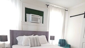 Ein ordentlich eingerichtetes Schlafzimmer mit einem großen Bett, zwei Nachttischen, einem Sessel und einem Fenster mit Vorhängen.