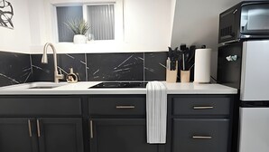 Eine moderne Küche mit dunklen Schränken, einer weißen Arbeitsplatte, einer Edelstahl-Spüle und einem Kühlschrank.