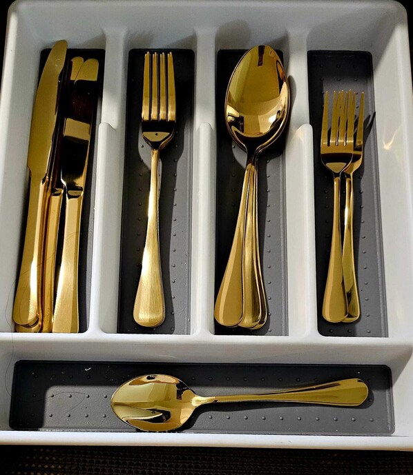 A set of gold-colored cutlery in a white tray with compartments.