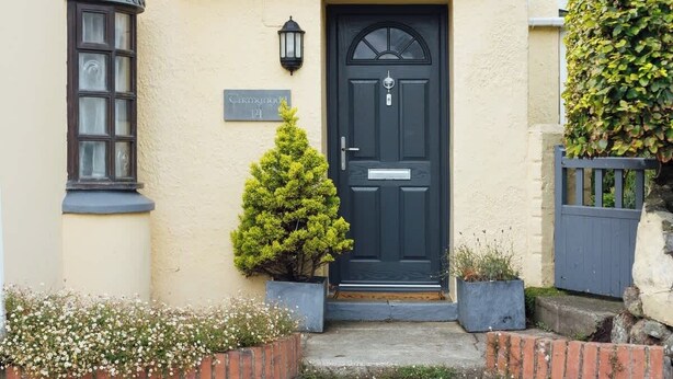 Una casa con una puerta principal oscura, un árbol pequeño en el frente y un letrero encima de la puerta.