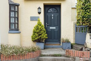 A house with a dark front door, a small tree in front, and a sign above the door. - Charming Upper Solva Cottage by Beaches & Harbour (Solfach)