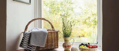 A window sill with a woven basket, a potted plant, a bowl of fruit, and a checkered cloth.