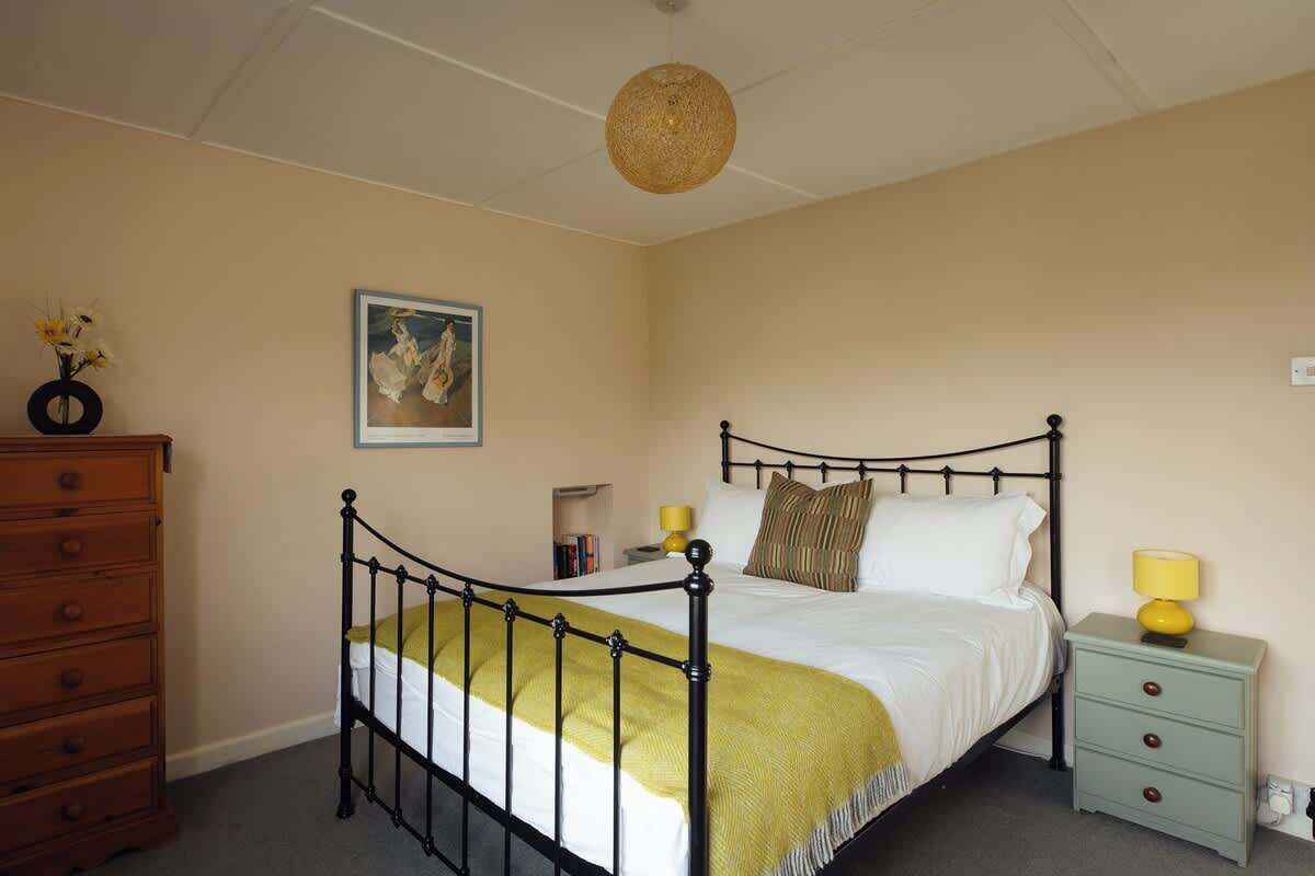A bedroom with a bed, a dresser, a nightstand, a lamp, and a painting on the wall.