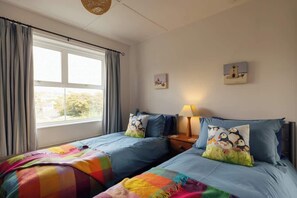 Camera da letto con due letti, una finestra con tende, un comodino con lampada e decorazioni alle pareti.